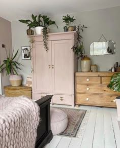 a bedroom with pink furniture and plants on top of the dresser in front of it