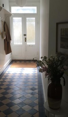 a vase with flowers sitting on the floor in front of a door and some coat racks