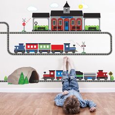 a child laying on the floor in front of a wall mural with trains and houses