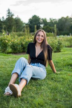 a woman sitting in the grass smiling at the camera with her legs crossed and head down