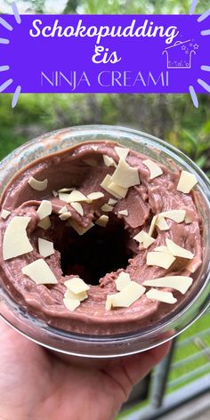 a hand holding a glass bowl filled with chocolate and marshmallows on top