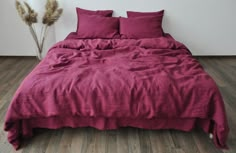 a bed with red sheets and pillows on top of wooden floor next to white wall