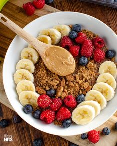 a white bowl filled with granola, berries and bananas on top of a wooden cutting board