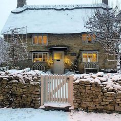 a stone house covered in snow next to a white fence