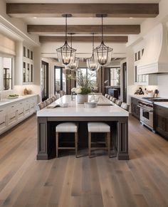 a large kitchen with wooden floors and white cabinets is pictured in this image, there are two chandeliers hanging from the ceiling