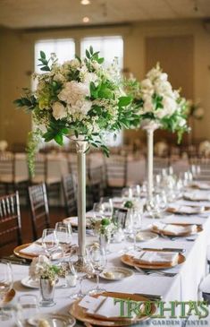 the tables are set with white and green flowers in tall vases on each table