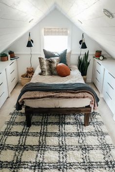 an attic bedroom with white walls, black and white rugs and lots of pillows