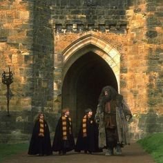 three people dressed in black and yellow robes are standing outside an old stone building with a large doorway