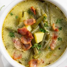 a white bowl filled with green beans, potatoes and ham in a creamy broth