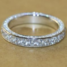 a wedding ring with three rows of diamonds on it's sides, sitting on a table