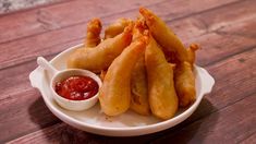 a white bowl filled with fried food on top of a wooden table next to dipping sauce