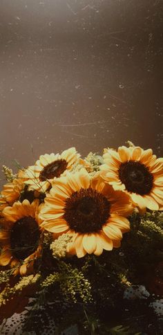 yellow sunflowers in a vase with moss and leaves on a table top, against a dark background