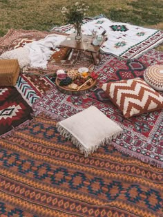 an outdoor picnic is set up on the grass with blankets, pillows and other items