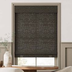 a living room with a large window covered in black roman blind blinds and a chair