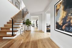 there is a painting on the wall next to the stairs in this house with wood flooring