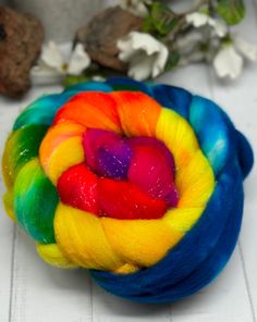 a multicolored ball of yarn sitting on top of a white table next to flowers