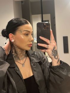 a woman with tattoos taking a selfie in front of a mirror while wearing a black shirt