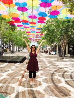 a woman is standing in the middle of an open area with colorful umbrellas overhead