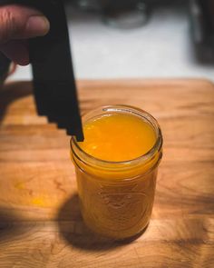 a person is holding a knife over a jar of orange juice on a cutting board