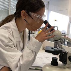 a woman in white lab coat looking through a microscope