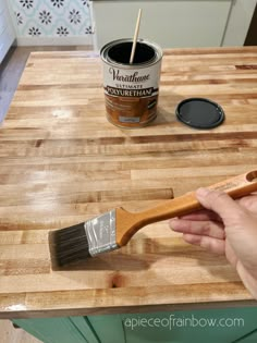 a person holding a paint brush on top of a wooden table next to a can