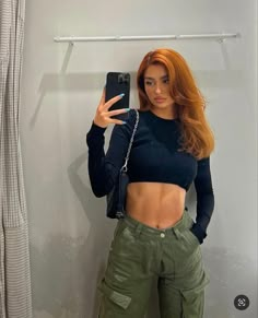 a woman taking a selfie in front of a mirror wearing green pants and a black crop top