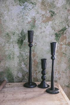 three black candlesticks sitting on top of a wooden table next to a wall