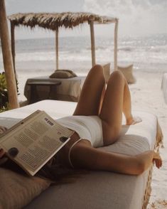 a woman laying on the beach reading a book