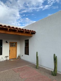 a white building with two cactus plants in front of it and a blue sky background