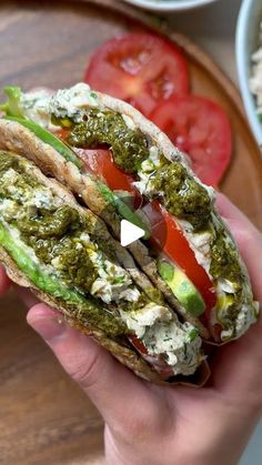 a hand holding a sandwich with pesto and tomatoes