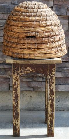 an old wooden stool with a woven hat on it's top sitting in front of a brick wall