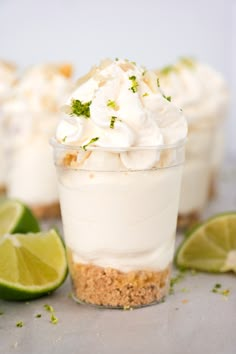 three small desserts with lime and whipped cream on top, surrounded by lime wedges