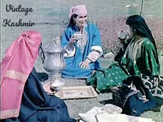 two women sitting on the ground talking to each other while one holds a teapot