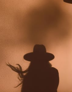 the shadow of a person with a hat on their head and hair blowing in the wind