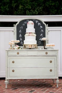 a wedding cake sitting on top of a white dresser next to a blackboard backdrop