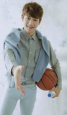 a young man holding a basketball in his right hand and pointing to the side with both hands