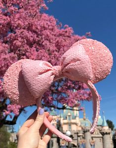 someone is holding up a pink bow headband in front of a tree with purple flowers