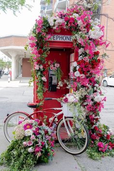 a bicycle parked next to a red phone booth with flowers on the front and side