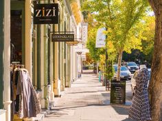 a woman is walking down the sidewalk in front of a clothing store on a sunny day