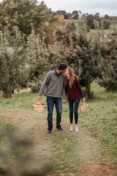 a man and woman walking through an apple orchard holding baskets with apples in them,