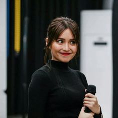 a woman holding a microphone in her right hand and looking at the camera with an intense smile on her face