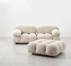 a white couch sitting on top of a floor next to a footstool in front of a wall