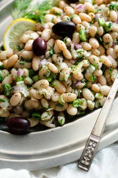 a white plate topped with beans and greens next to a lemon wedge on a table