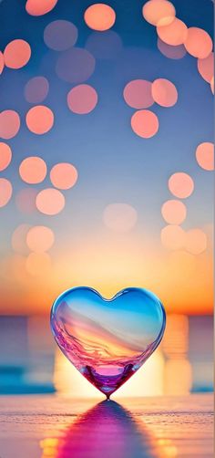 a heart shaped glass object sitting on top of a table next to the ocean at sunset