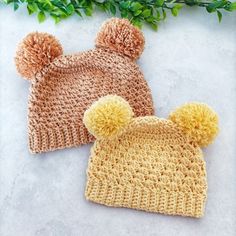 two crocheted hats with yellow and brown pom - poms on them