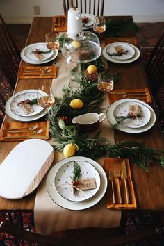 the table is set for christmas dinner with plates, silverware and pine cones on it