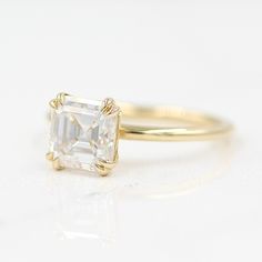 a yellow gold ring with an emerald cut diamond in the center on a white surface