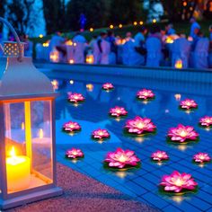 many lit candles are on the ground near a pool with water lilies in it