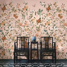 two chairs sitting next to each other in front of a wall with flowers on it