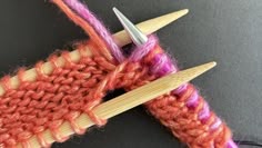 an orange and pink knitted object with two crochet needles in the middle